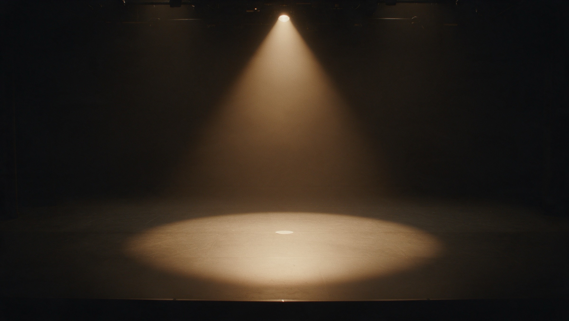 An empty black-box stage, one spotlight hitting the mark at center stage